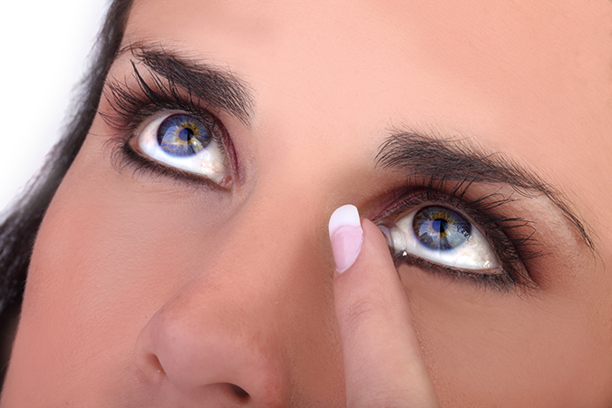 A blue eyed woman putting in her contact lenses