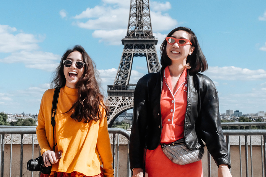 Two beautiful woman wearing sunglasses standing in front of the Eiffel Tower