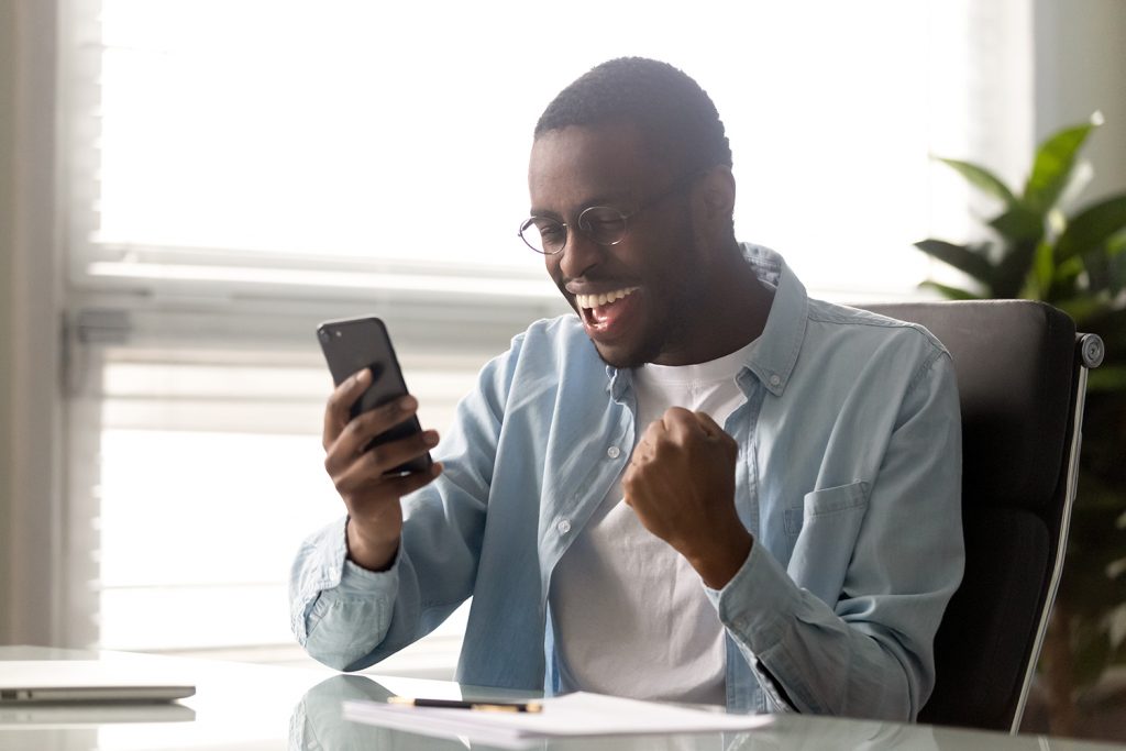 A handsome black man wearing glasses looking at his cellphone and smiling