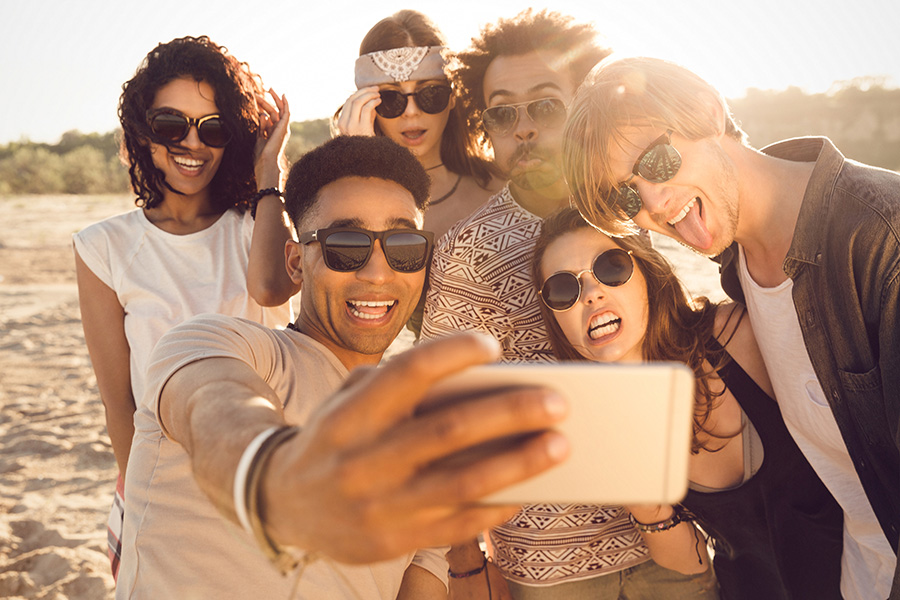multiracial group of friends wearing sunglasses and taking selfies