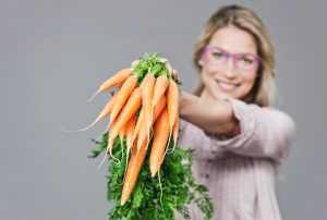 adult woman with purple glasses holding carrots